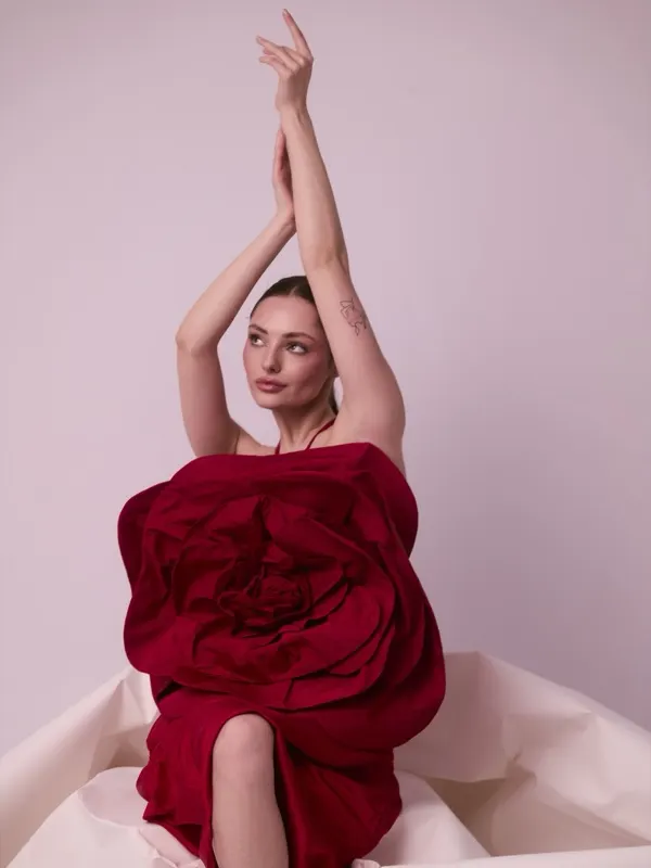 Women's photo session Wroclaw — Julia arms raised in sculptural red flower dress, pink background, artistic pose