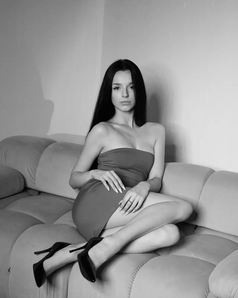 Nikola w czarnej sukience bez ramiączek siedząca na kanapie, czarno-biały portret